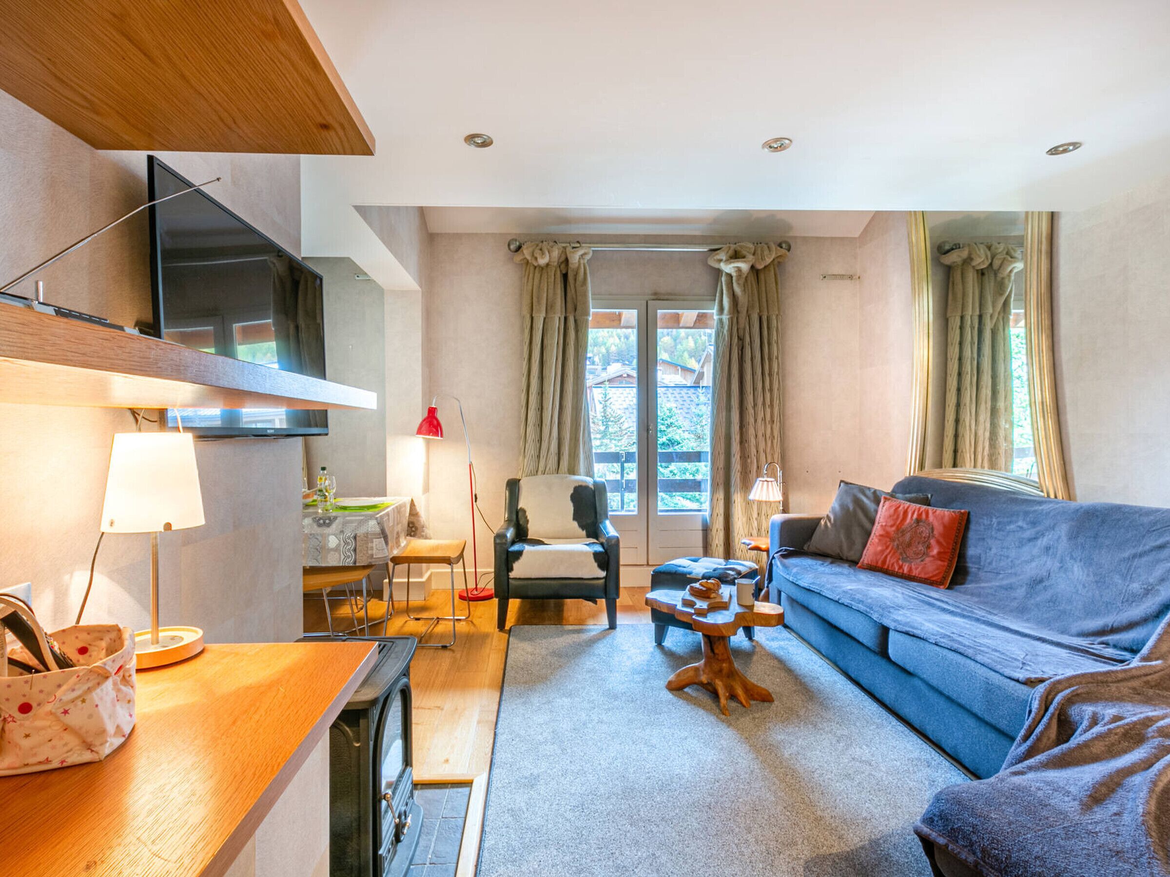 A cozy living room with a sofa, a wooden coffee table, a TV mounted on the wall, and a dining area with a table and chairs.