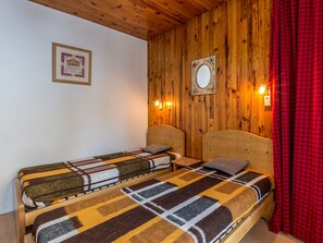 A room with wooden walls, a bed with a patterned blanket, a framed mirror, and two wall-mounted lights.