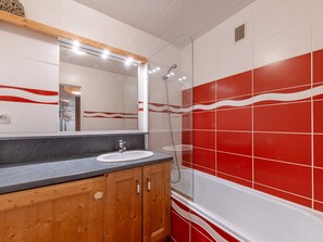 A bathroom with a wooden vanity, a white sink, and a shower area with red tiles.