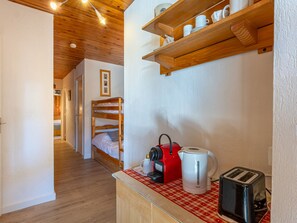 A narrow hallway with wooden flooring, a bunk bed, a kitchenette with a red kettle, a white coffee maker, and a toaster.