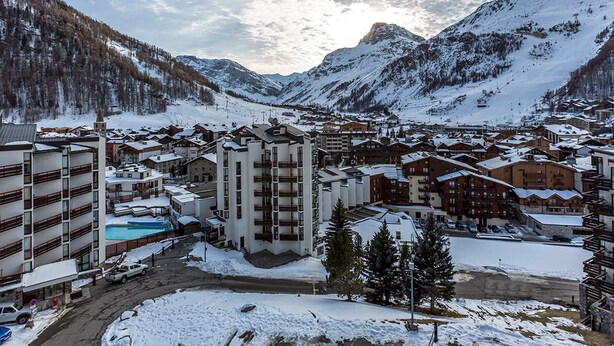 A snow-covered mountain town with buildings, a swimming pool, and a ski slope.