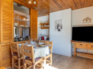 A wooden dining table with chairs, a television, and a shelf with kitchenware.