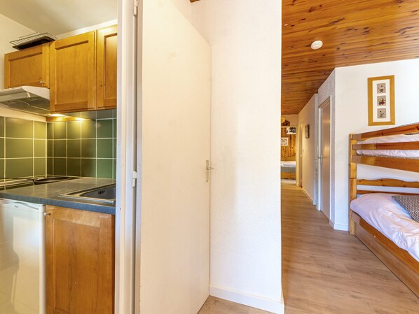 A narrow hallway with a wooden door leading to a kitchen with wooden cabinets and a tiled backsplash.