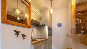 Eine schmale Küche mit Holz Arbeitsplatte, Edelstahlspüle und integriertem Backofen. Es befinden sich Pendelleuchten an der Decke und ein Spiegel über der Spüle.