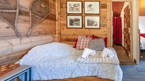 Ein gemütlicher Holzraum mit einem Bett, gerahmten Bildern an der Wand und einem Korbsessel.