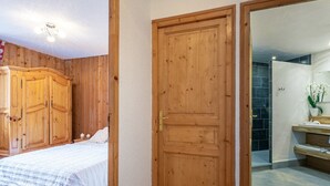 A bedroom with a bed, wooden wardrobe, and a bathroom with a sink and mirror. - Rustic Mountain-Style Apartment in Chalet, Village Center, Ski-In/Ski-Out (Val-d'Isère)