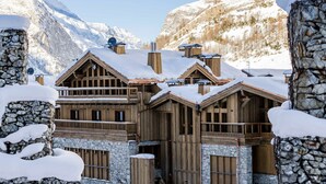 A wooden chalet with stone walls, multiple balconies, and a mountain backdrop. - Elegant Apartment in New Residence with Ski-in/Ski-out Access in Val-d'Isère (Val-d'Isère)