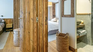 A room with a wooden wardrobe, a bed with white bedding, a bedside table, a woven basket, and a bathroom with a stone sink and towel rack. - Elegant Apartment in New Residence with Ski-in/Ski-out Access in Val-d'Isère (Val-d'Isère)