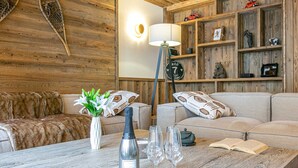 A cozy living room with a wooden wall, a sofa, a coffee table with a bottle and glasses, and a lamp. - Elegant Apartment in New Residence with Ski-in/Ski-out Access in Val-d'Isère (Val-d'Isère)