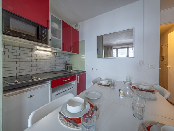 A compact kitchen with a microwave, red cabinets, and a dining table set with plates and glasses.