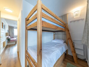A bunk bed with a wooden frame and white bedding, a radiator, and a wall-mounted light fixture.