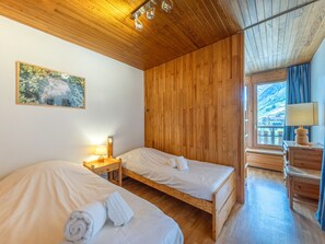 Ein Zimmer mit zwei Betten, Holzwänden, einem Fenster mit Blick und einem Nachttisch mit Lampe sowie einer Kommode.