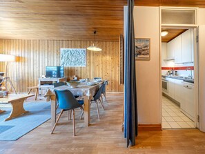 A dining area with a wooden ceiling, a table set for four, and a kitchen visible through an open door. - Comfortable south-facing apartment with balcony and washing machine (Val-d'Isère)