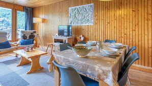 Ett rum med träpanel på väggarna, ett matbord för fyra personer, en tv och ett fönster med gardiner.