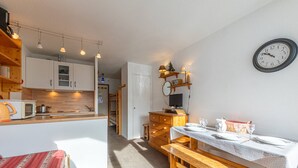 Eine kompakte Küche mit Mikrowelle, Herd und Holzausstattung. Es gibt einen Essbereich mit einem Tisch für zwei Personen und einer Uhr an der Wand.