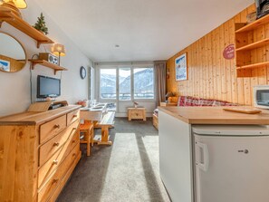 A cozy, well-lit kitchen with wooden cabinets, a dining table, and a view of snowy mountains through large windows.