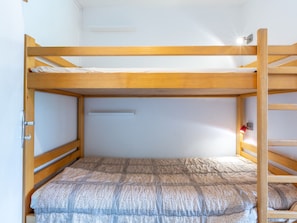 A bunk bed with a wooden frame, a white wall, and a small shelf.