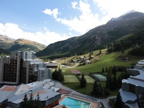 Een modern hotel met een zwembad, tennisbanen en uitzicht op een bergachtig landschap.