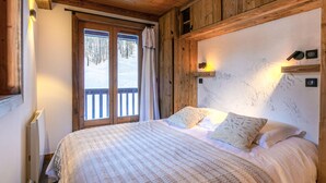 Une chambre confortable avec un grand lit, un plafond en bois et une vue sur un paysage enneigé, visible à travers une porte coulissante.