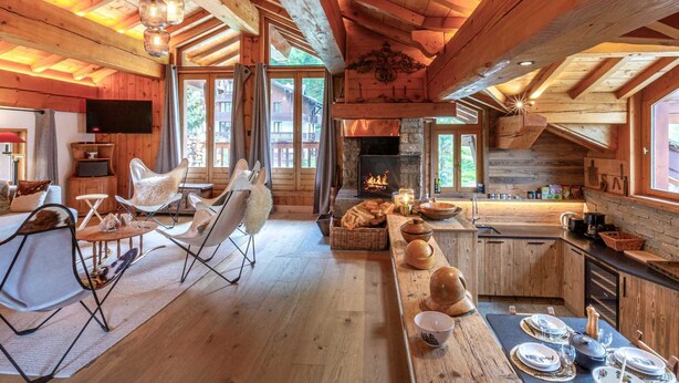 L’intérieur chaleureux d’un chalet avec un plafond en bois, une cheminée, un coin repas et un salon équipé d’un téléviseur et de sièges confortables.