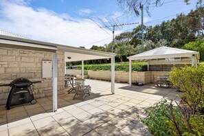 Un espace extérieur aménagé en patio, avec un barbecue, des sièges et une partie abritée.