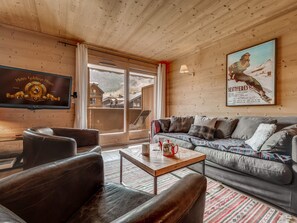 A cozy living room with a leather sofa, a coffee table, and a television on the wall.