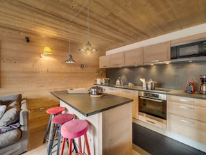 A modern kitchen with wooden walls, a central island, bar stools, and stainless steel appliances. - Luxurious 4-Room Apartment with South-Facing Balcony in Central Val-d'Isère (Val-d'Isère)