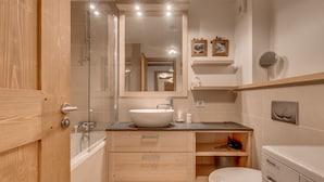 Ein modernes Badezimmer mit Duschkabine aus Glas, einem weißen Waschbecken, Holzschränken, einer Toilette und einer integrierten Waschmaschine.