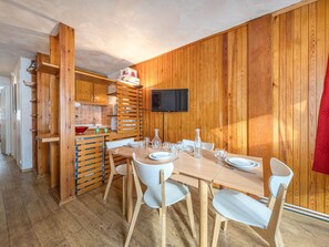 A wooden-paneled room with a dining table set for four, a kitchen area with wooden cabinets, and a flat-screen TV mounted on the wall.