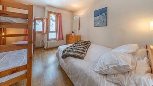 Une chambre avec un lit superposé, un lit simple, une commode, un miroir et un tableau accroché au mur.