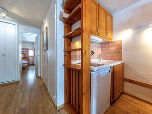 A compact kitchen with wooden cabinets, a built-in dishwasher, and a tiled backsplash.
