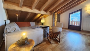 Ein gemütliches Schlafzimmer unter dem Dach mit Holzbalkendecke, einem Bett, einem Sessel und einem kleinen Tisch mit Lampe.
