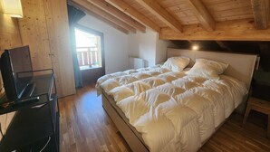 Ein Schlafzimmer mit Holzbalkendecke, einem Bett mit weißer Bettwäsche, einem Schreibtisch mit Computer und einem Fenster mit Blick.