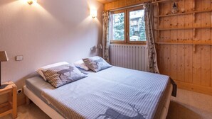 Una habitación con paneles de madera, una cama, dos lámparas de pared, un ventanal con cortinas y un radiador.