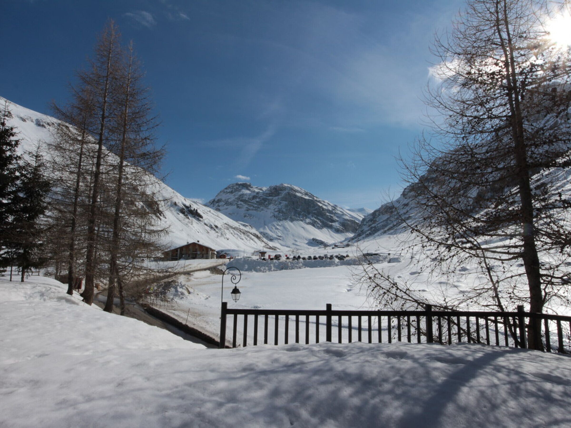 Un paysage montagneux enneigé, avec une cl ôture en bois, un petit bâtiment et des arbres sans feuilles.