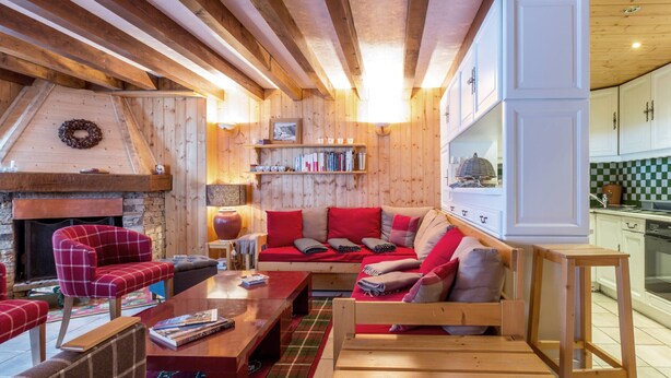 Una sala de estar acogedora con chimenea, muebles de madera y una cocina visible al fondo.