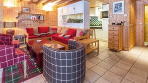 Interior acogedor de una cabaña con techo de madera, un conjunto de sofás, una mesa de comedor y una zona de cocina.
