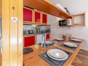 Cozinha compacta com armários vermelhos, micro-ondas e área de refeições com pratos e copos.