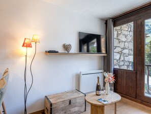 A modern living room with a flat-screen TV, a stone wall, a wooden chest, and a table with a bottle and glasses. - Renovated ski-in/ski-out apartment with parking and wifi in Val-d'Isère (Val-d'Isère)