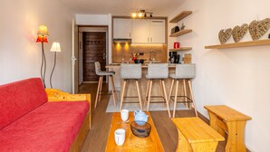 Un espace de vie compact comprenant un coin cuisine, un canapé rouge, une table basse en bois et un petit coin repas.