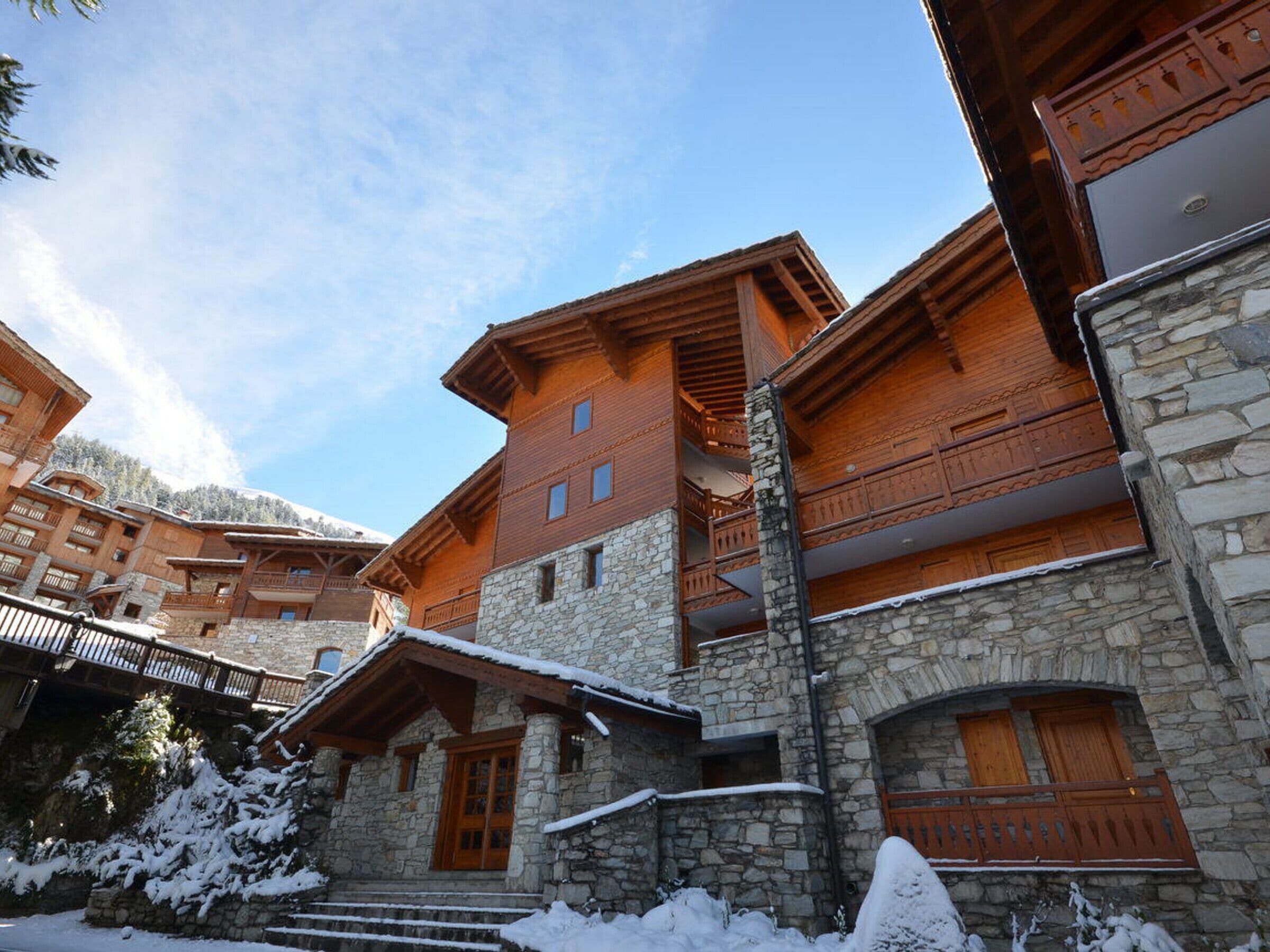 A multi-story hotel with stone and wooden architecture, featuring balconies and a stone staircase leading to the entrance.