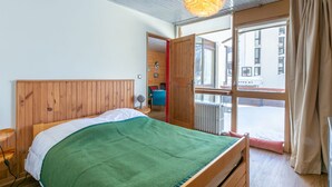 Un dormitorio con cabecera de madera, manta verde, mesita de noche y ventana con cortinas.