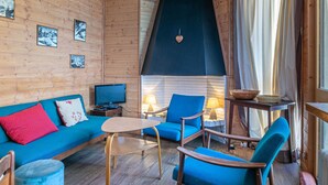 Un interior de cabaña acogedor, con pared de madera, un sofá azul, una mesita y dos sillones azules.
