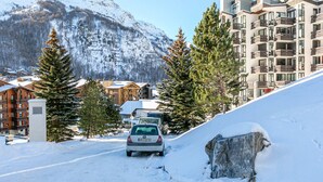 Carretera de montaña nevada con un automóvil, edificios de madera y un moderno edificio de apartamentos con balcones.