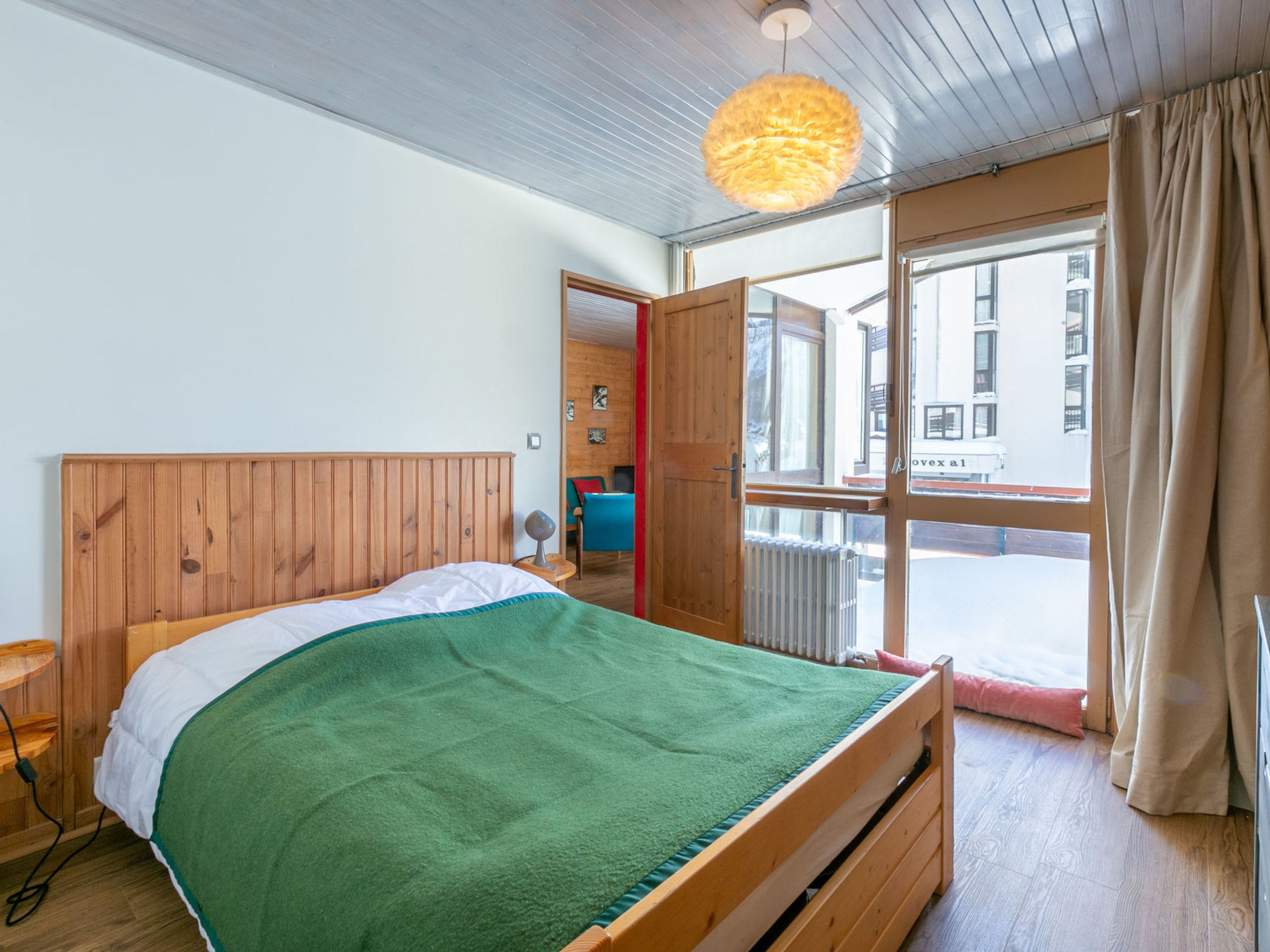 Een slaapkamer met een houten hoofdbord, een groene deken, een nachtkastje en een raam met gordijnen.