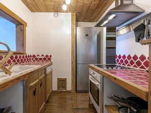 A compact kitchen with wooden cabinets, a stainless steel refrigerator, and a tiled backsplash. - Charming 3-Room Apartment with WiFi, Ski Shuttle Access, Mountain Views (Val-d'Isère)