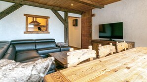 A cozy room with a wooden ceiling, a black leather sofa, a wooden dining table, and a television. - Charming 3-Room Apartment with WiFi, Ski Shuttle Access, Mountain Views (Val-d'Isère)