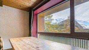 A wooden table in a room with a large window overlooking a mountainous landscape. - Charming 3-Room Apartment with WiFi, Ski Shuttle Access, Mountain Views (Val-d'Isère)