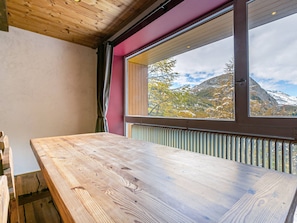 A wooden table in a room with a large window overlooking a mountainous landscape.