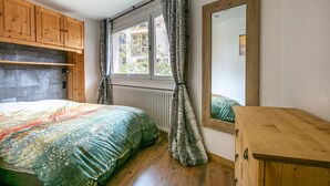 A bedroom with a bed, wooden cabinets, a window with curtains, a radiator, and a mirror. - Charming 3-Room Apartment with WiFi, Ski Shuttle Access, Mountain Views (Val-d'Isère)